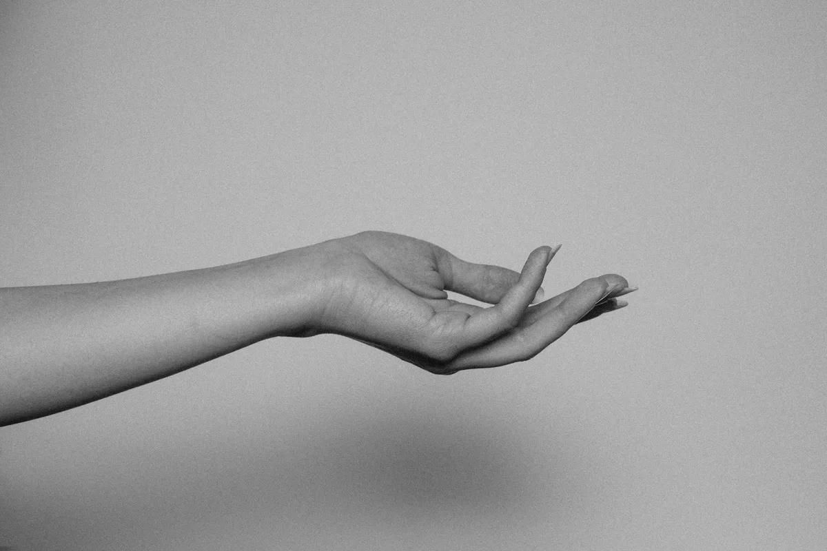 Black and white photograph of a woman's bare forearm and open hand held out against a plain background.