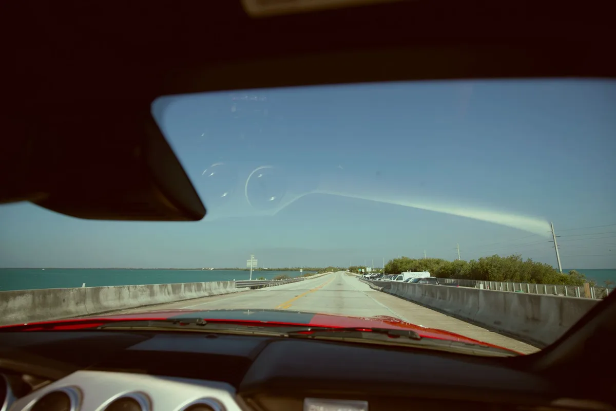 View through a car windshield of a long bridge over open water under a clear sky.