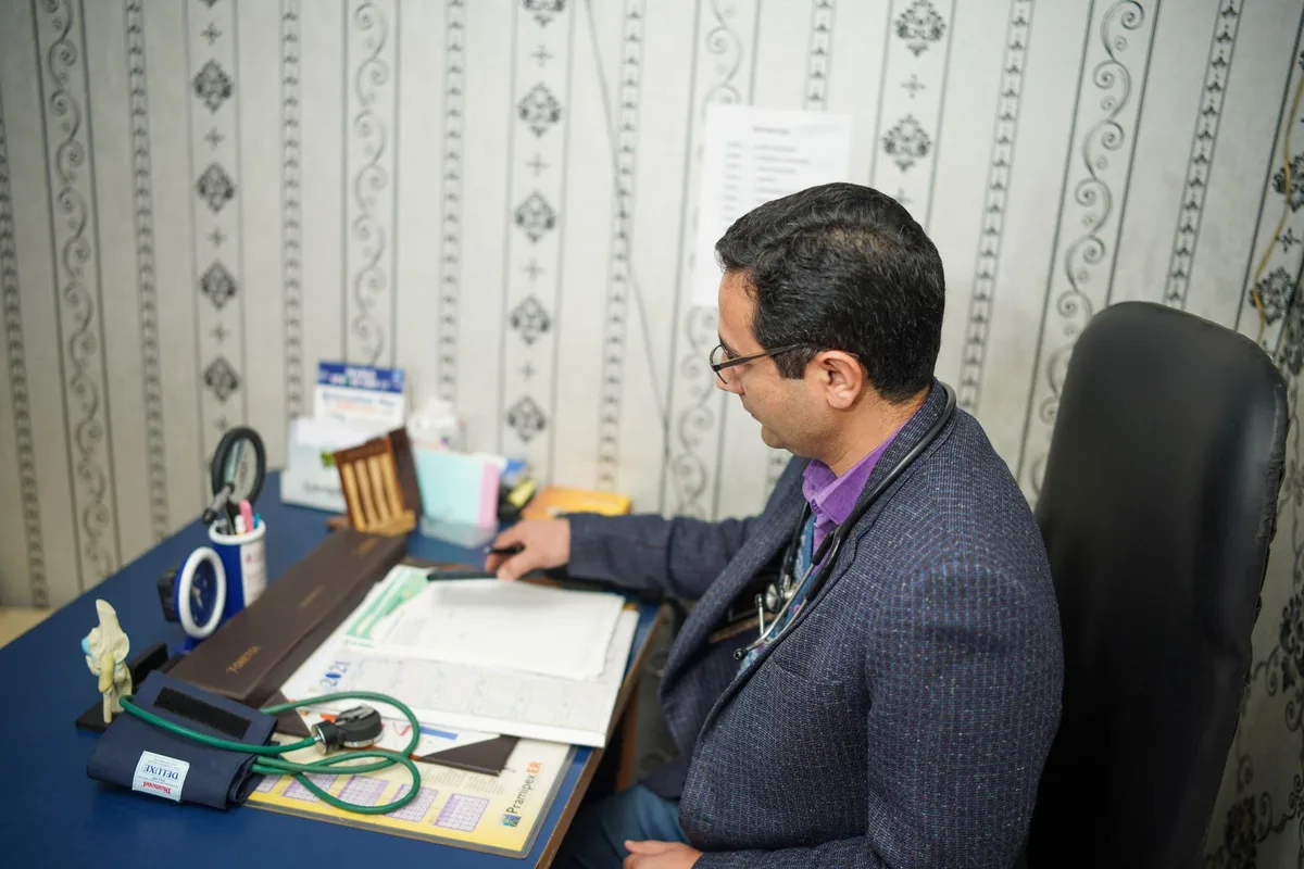 A physician reviewing a folder of medical records at a desk in a clinic office.