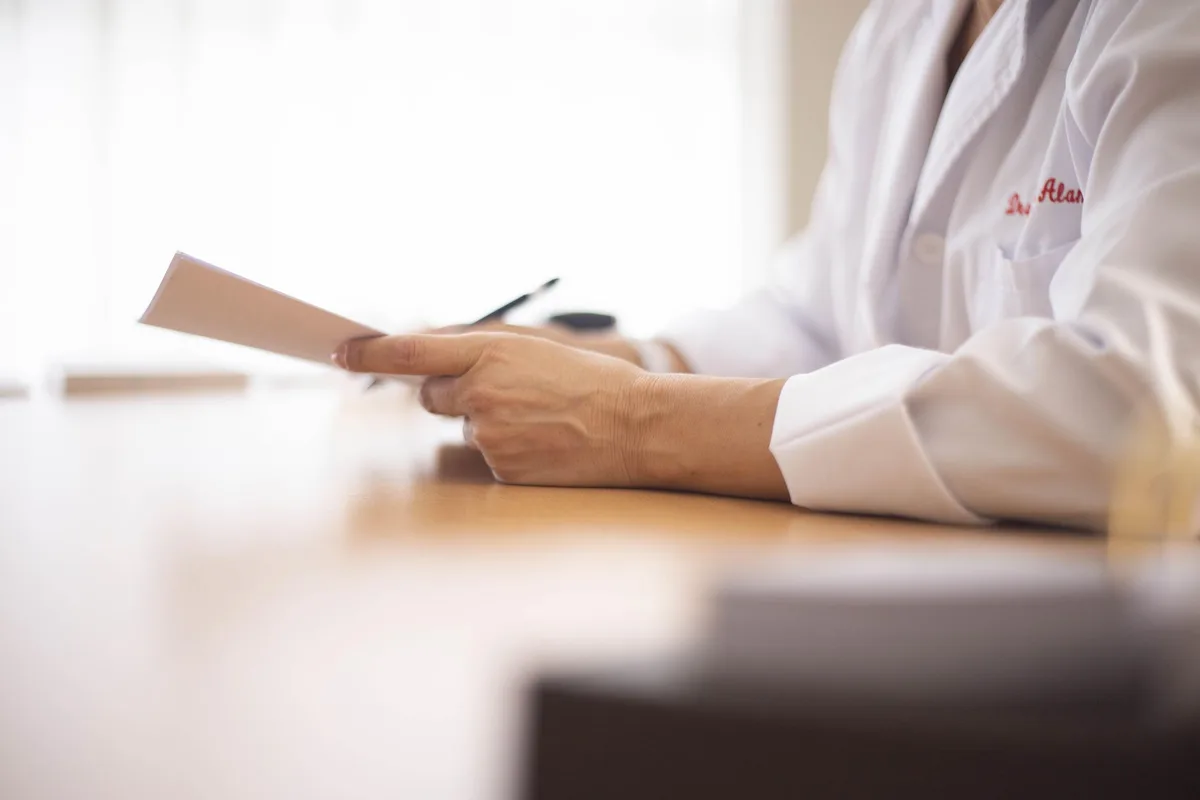 Close view of a physician in a white coat reading a printed letter at a desk.