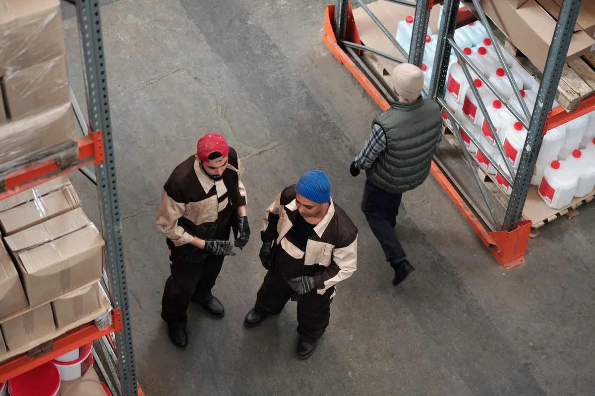 High-angle view of warehouse workers standing on a concrete floor between storage racks.