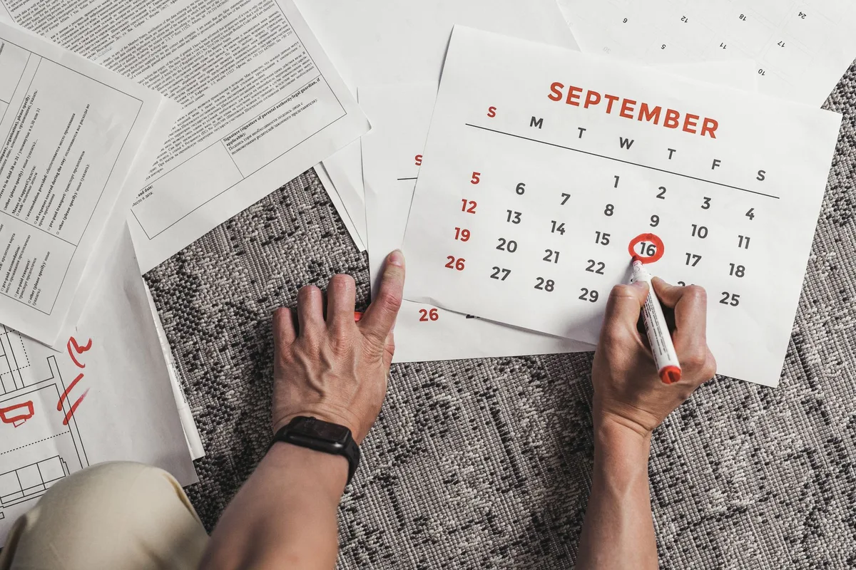 Hands holding a paper calendar with several September dates circled in red, papers spread around it.