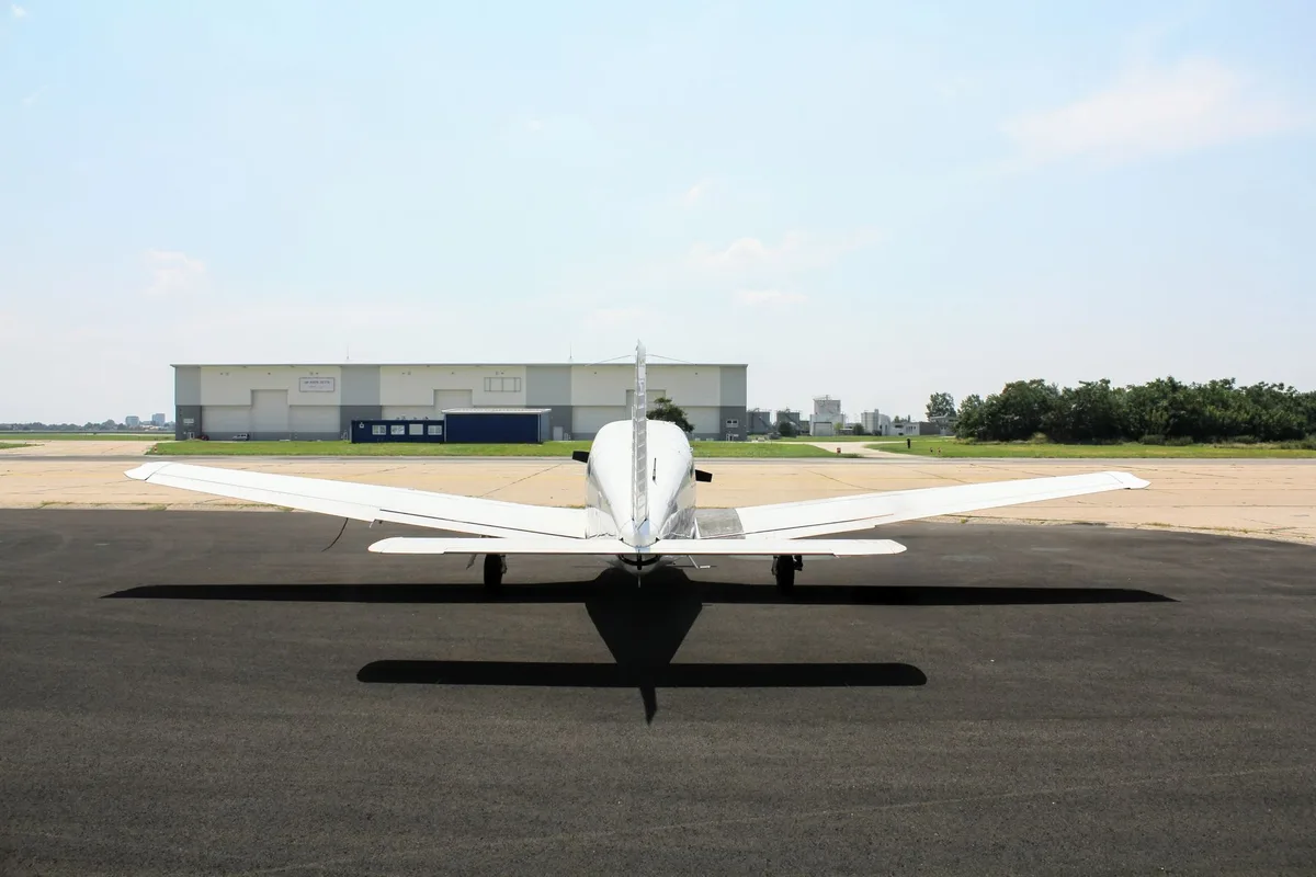 A small single-engine aircraft parked on a regional airport runway with hangars behind it.
