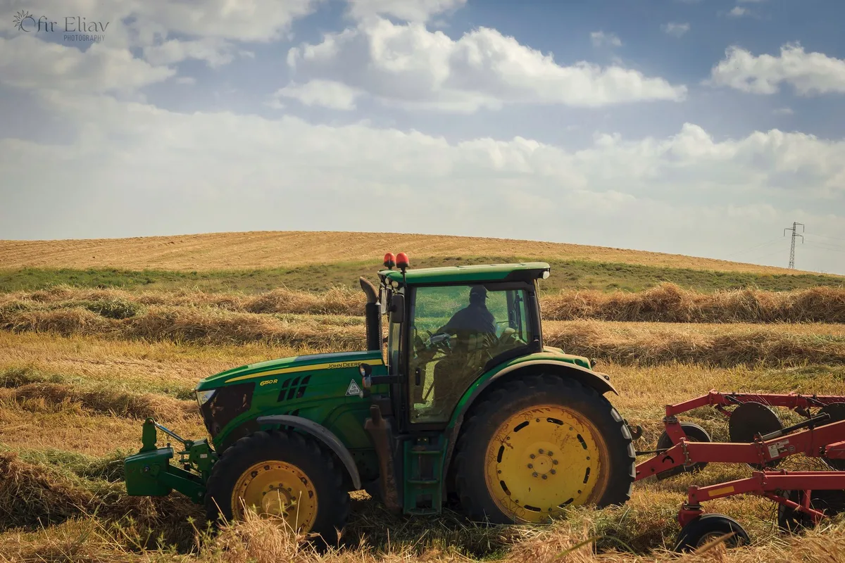 A green tractor pulling a mower through a hay field under a blue sky.