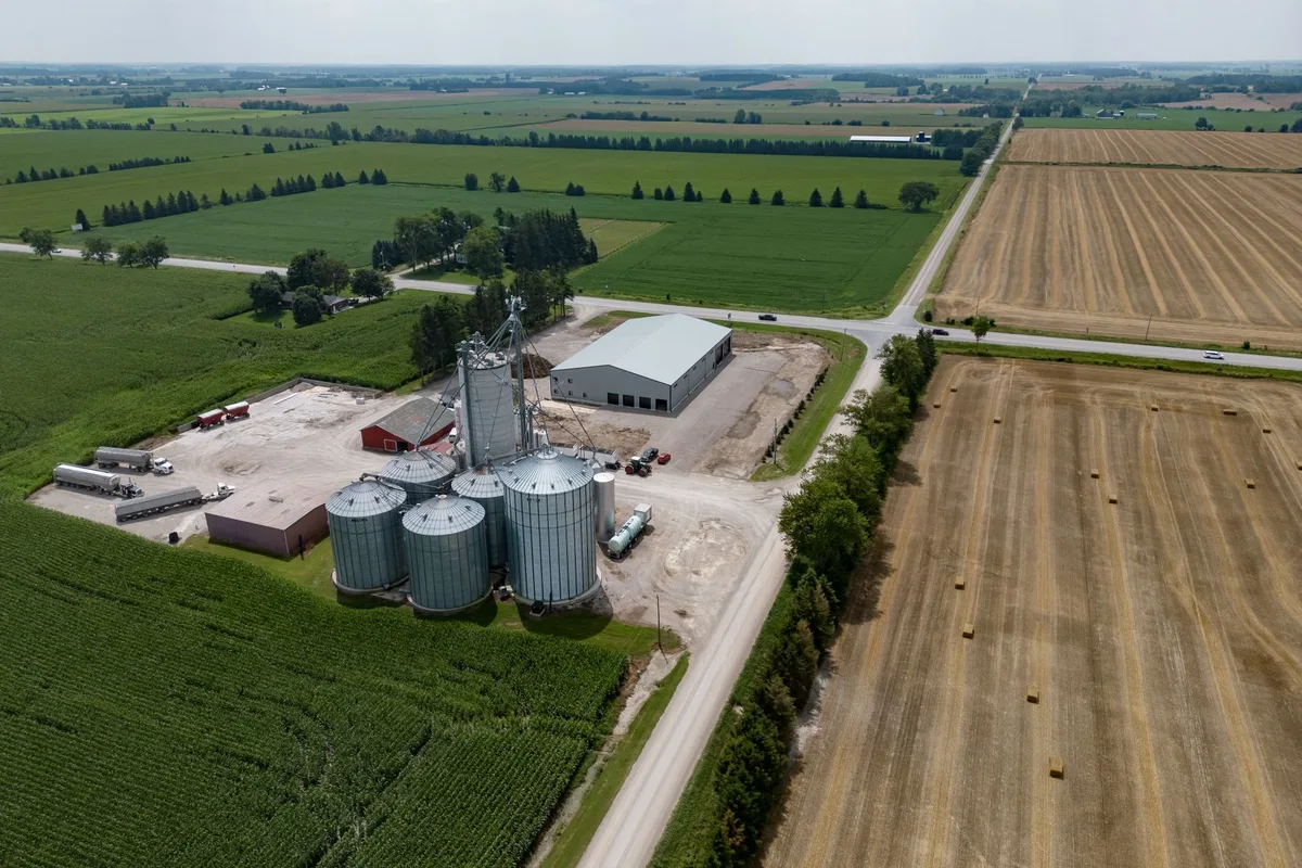 Aerial view of farmland with a cluster of grain bins beside a rural road.