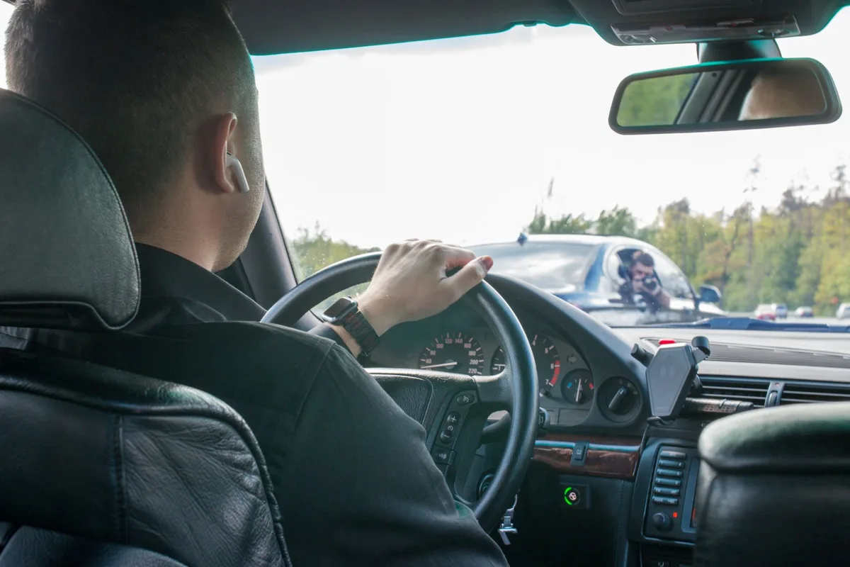 A driver seen from the back seat with both hands on the wheel in highway traffic.
