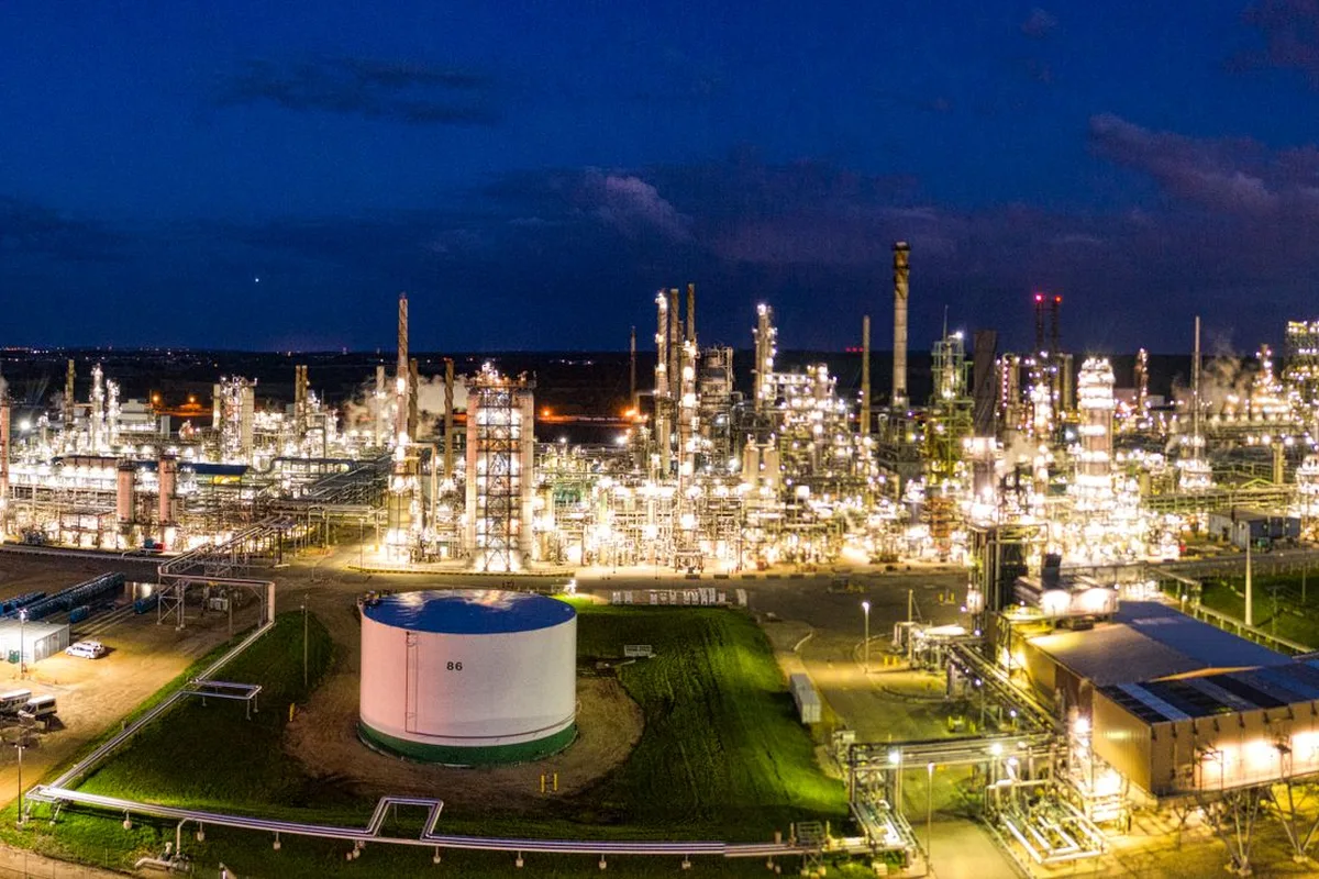 Aerial night view of a refinery lit up, with stacks and storage tanks.