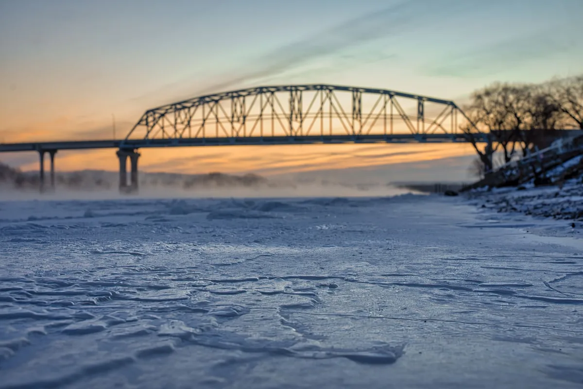 A steel bridge over the frozen Mississippi River at sunset in winter.