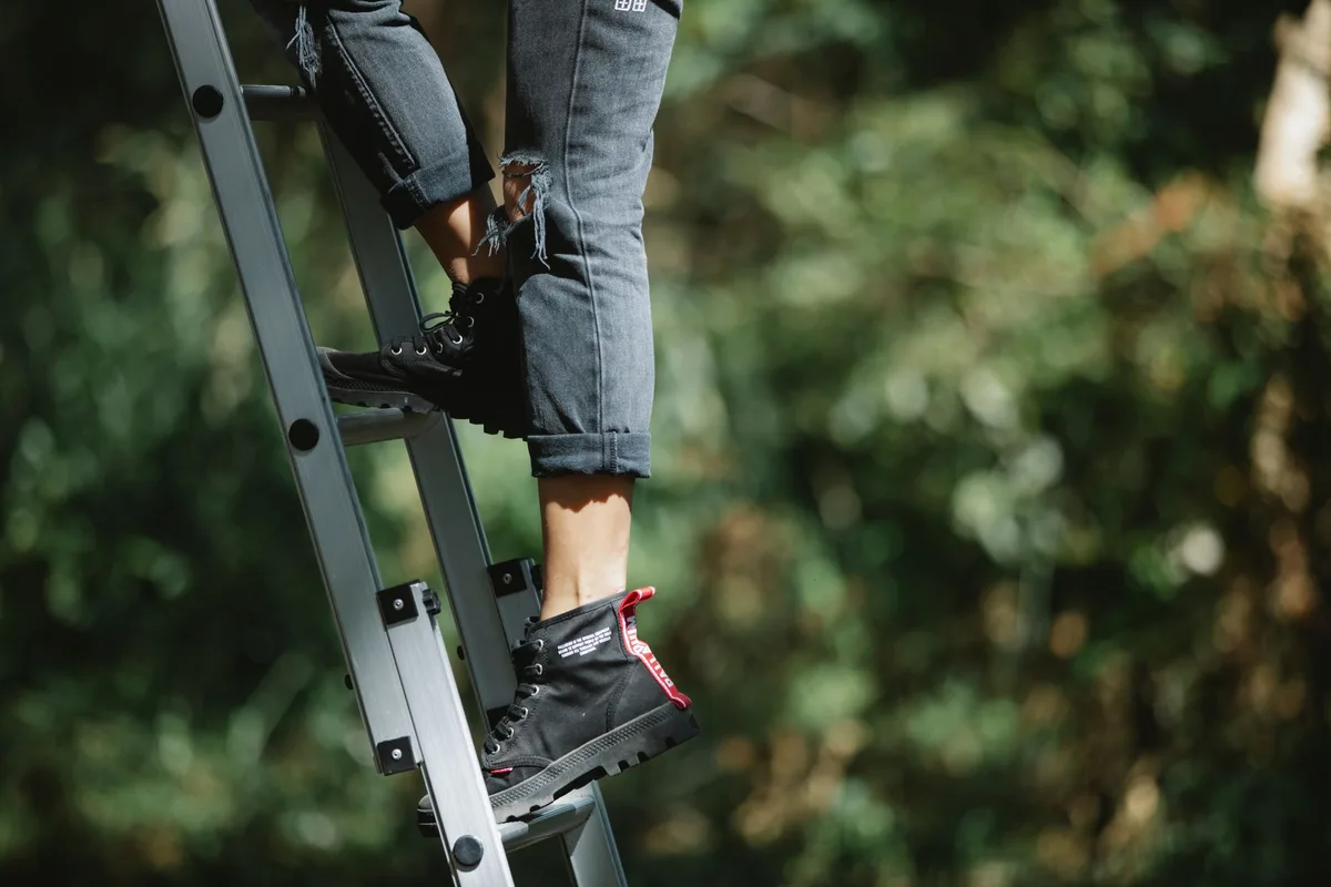 A person in work boots and jeans stepping down a metal ladder, one foot landing first.