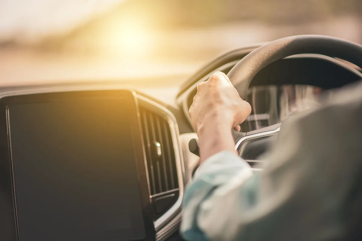 A driver's hands on the steering wheel with sunlight streaming through the windshield.