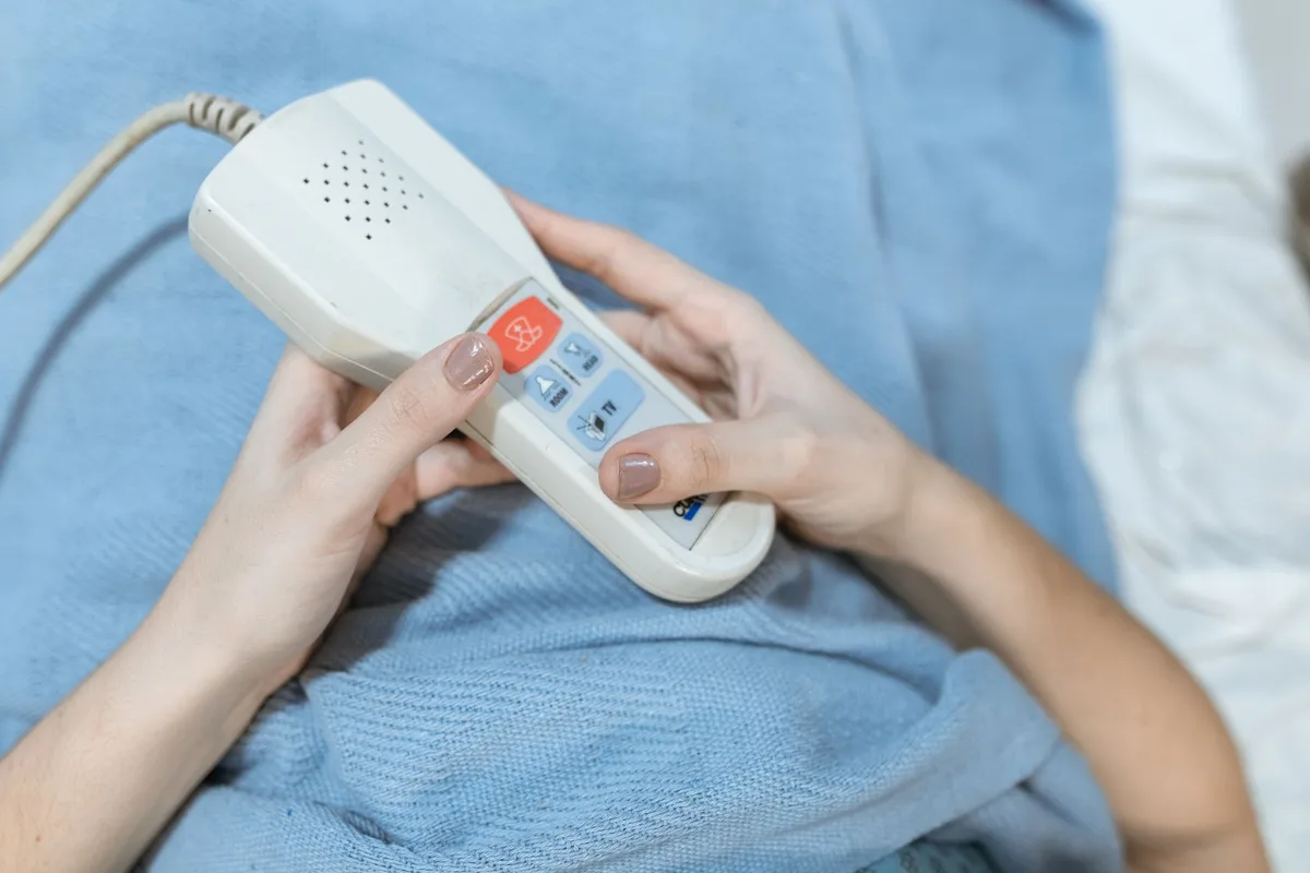 A patient's hands holding a small handheld control device over a blue blanket.