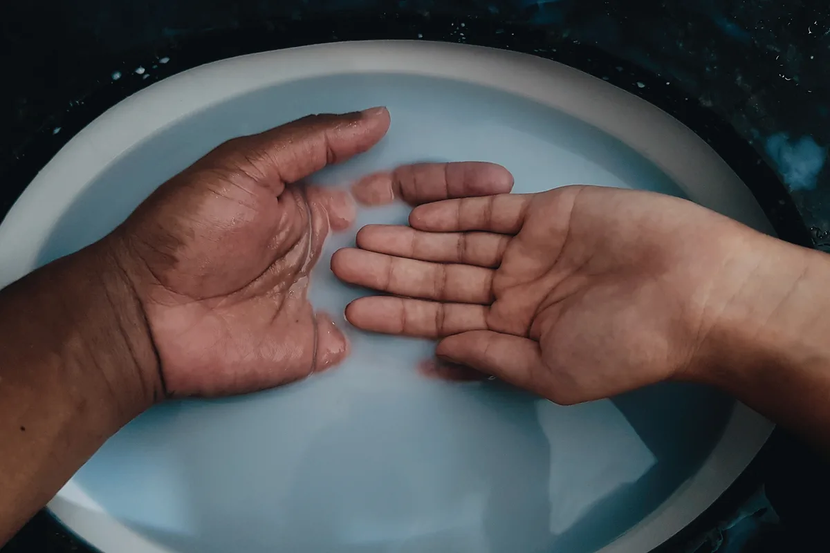 Two hands held side by side under water in a white basin.