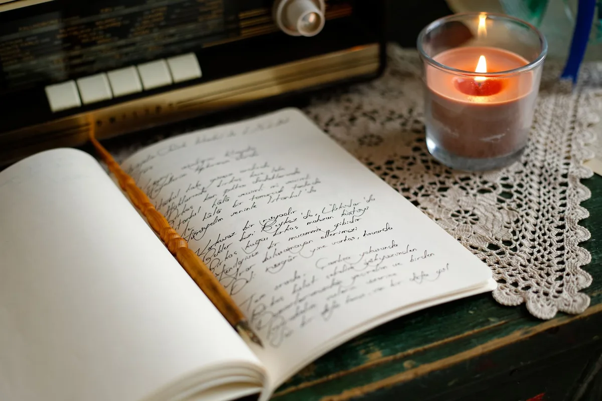 An open notebook of handwritten notes on a lace tablecloth beside a lit candle.