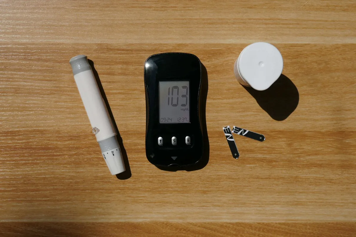 A blood glucose meter, lancet pen and test strips laid out on a wooden table.