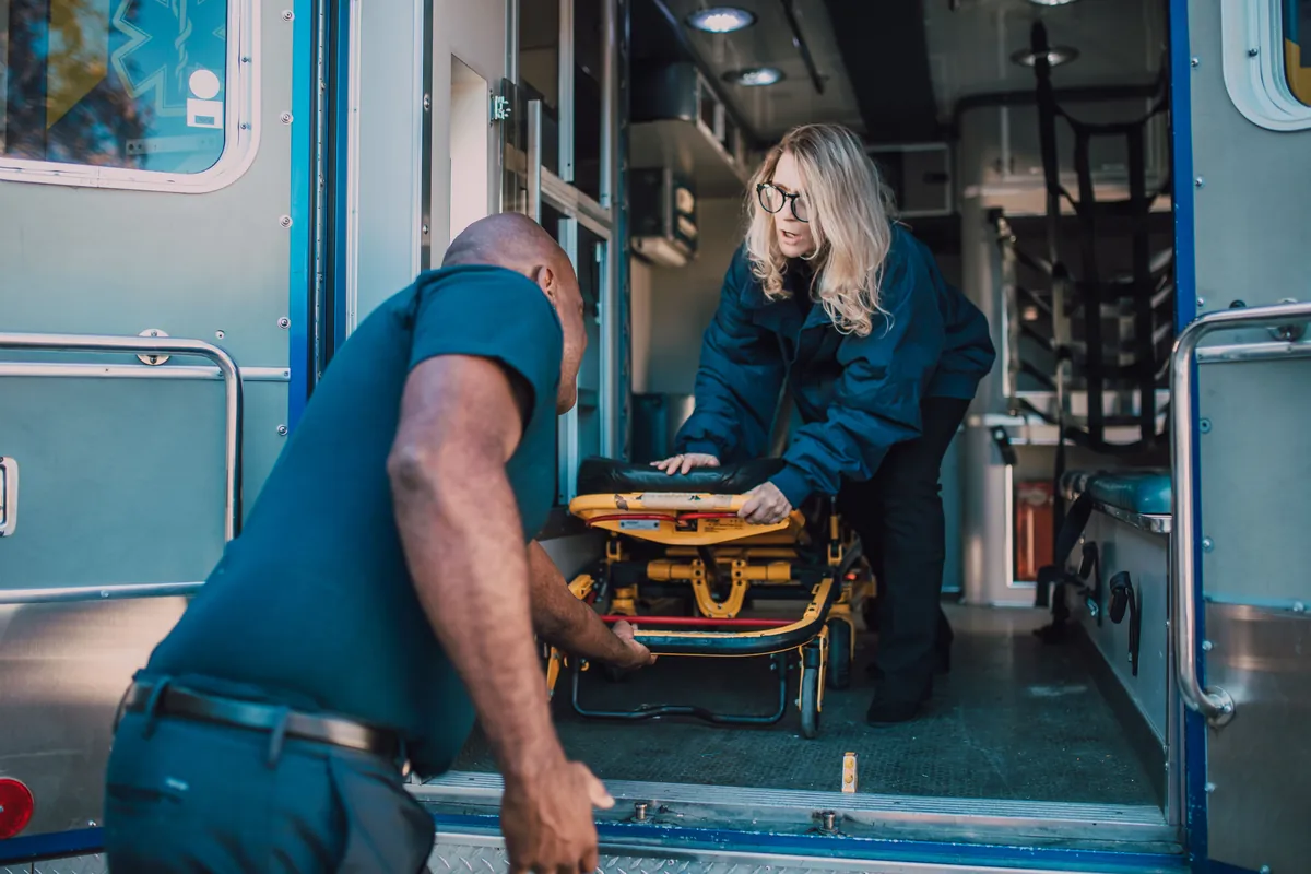 Two paramedics loading a stretcher into the back of an ambulance.
