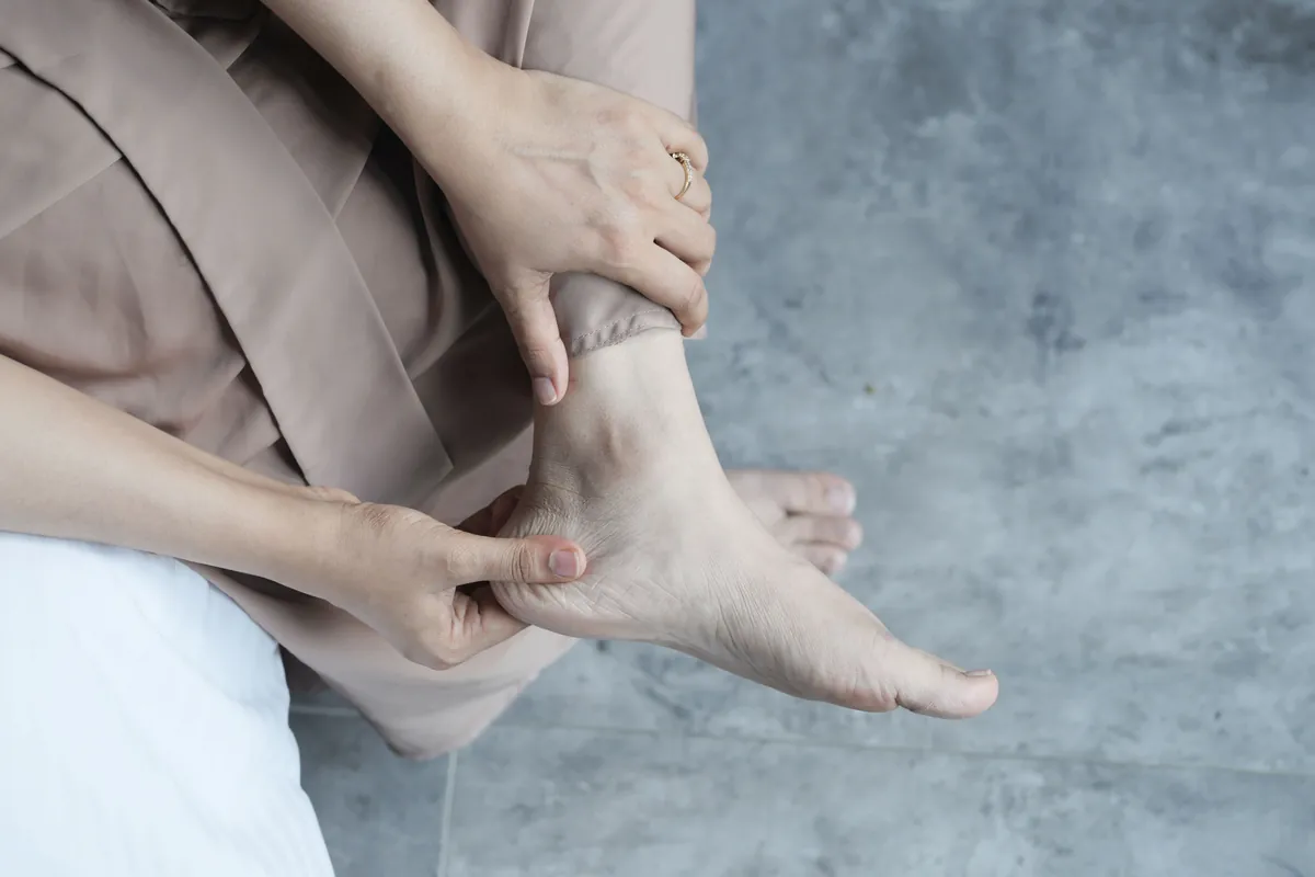 A seated person holding a bare foot and ankle with both hands.