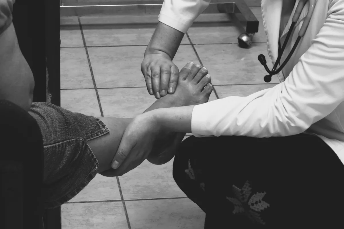 A clinician holding and examining a patient's bare foot, shown in black and white.