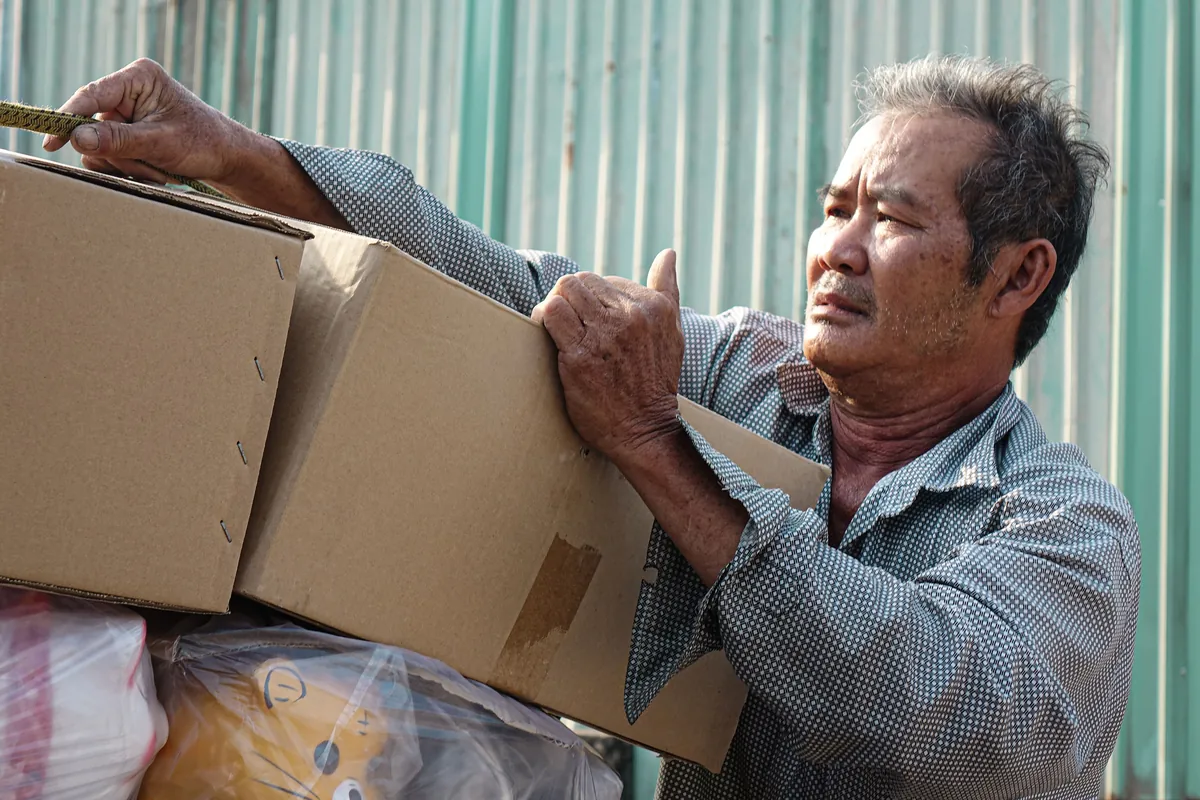 An older worker lifting a stack of cardboard boxes on the job.