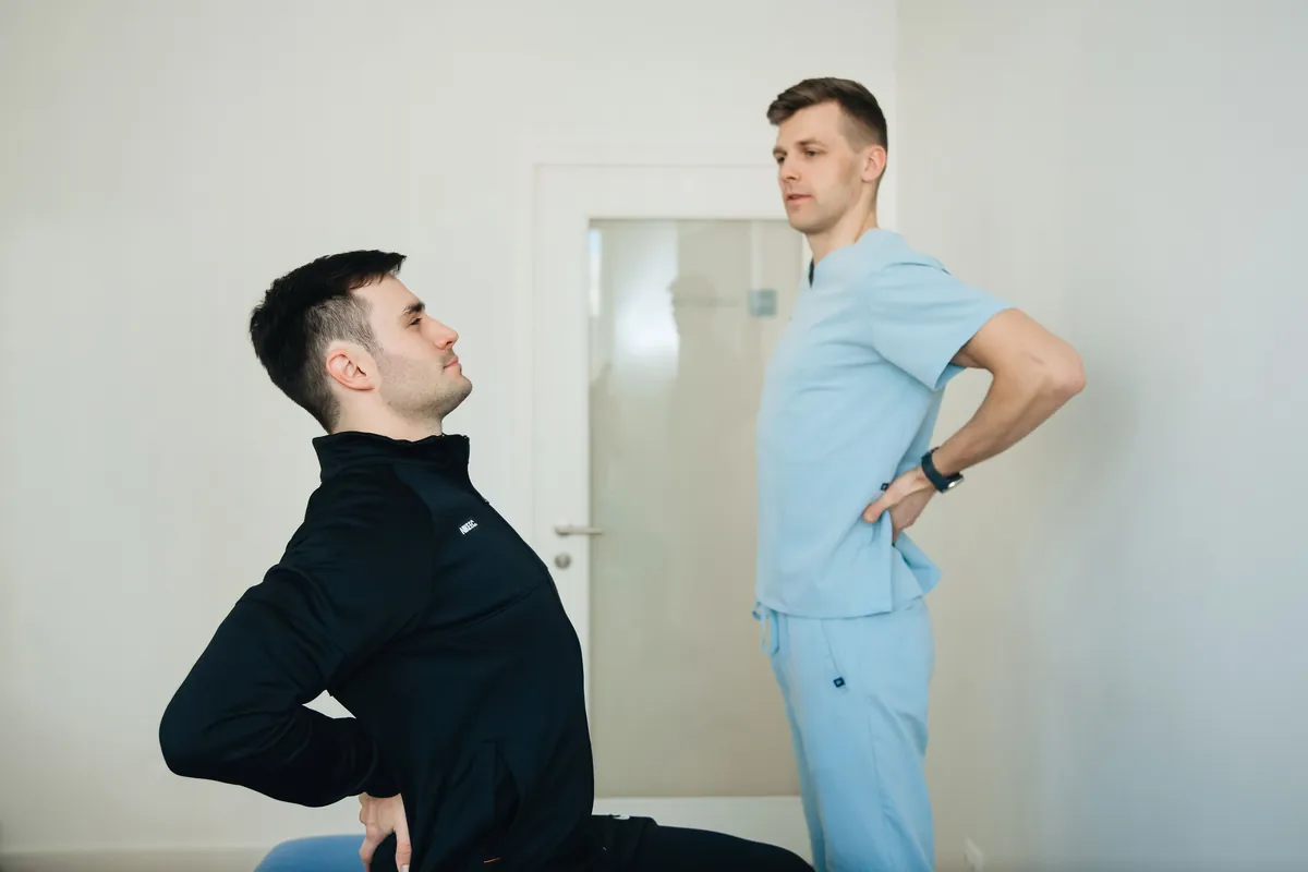 A clinician watching a patient lean back with his hands on his lower back during a movement exam.