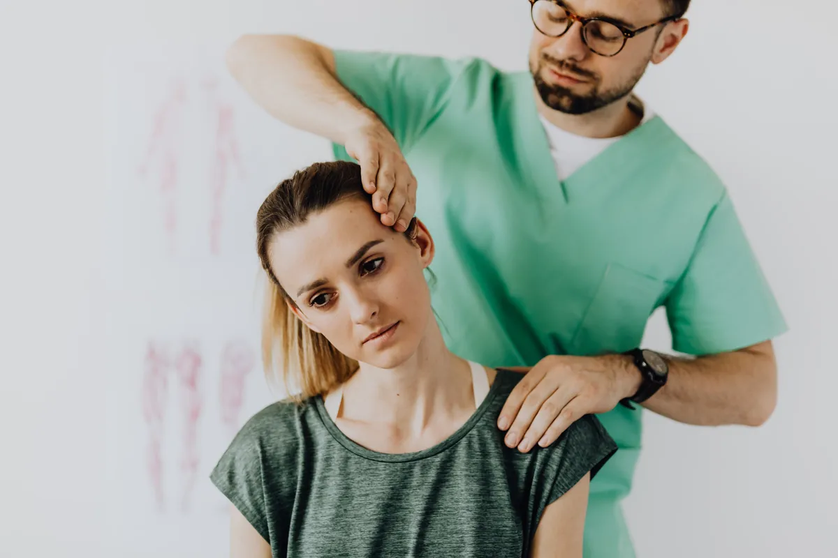 A clinician pressing along the back of a woman's head and neck to find the tender spot.