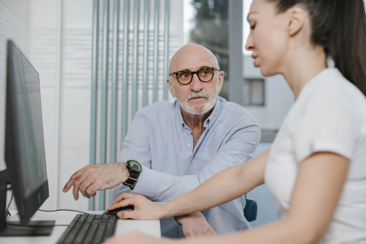An older man going over his records on a computer screen with a clinician at a desk.